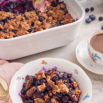 Pinterest graphic of a bowl of blueberry crisp with a baking dish with the rest of the crisp in the background.