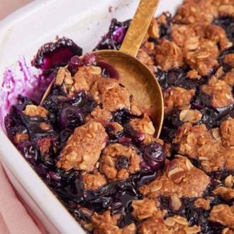 A spoon tucked under a serving of blueberry crisp in a baking dish.