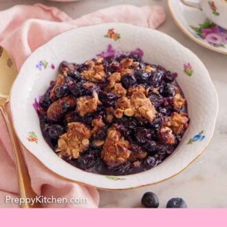 Pinterest graphic of a bowl of blueberry crisp with a cup of tea and second bowl in the background.