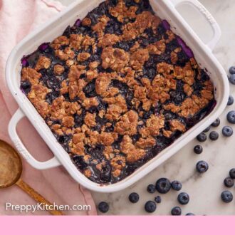 Pinterest graphic of an overhead view of blueberry crisp in a white baking dish with blueberries scattered around.
