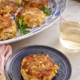 Pinterest graphic of a plate with a crab cake and a platter with more in the background with wine.