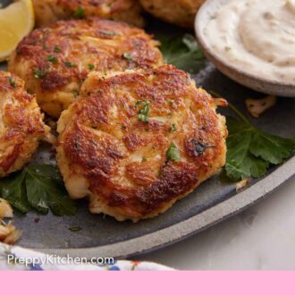 Pinterest graphic of a platter of crab cakes with tartar sauce, lemon wedges, and parsley.