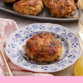 Pinterest graphic of a small plate with a crab cake and platter of more crab cakes in the background.