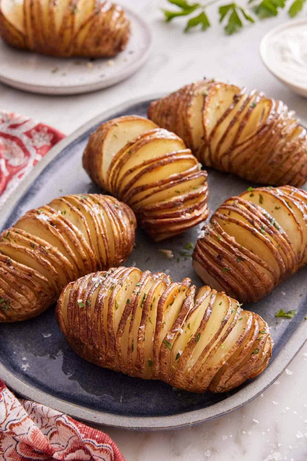A platter with five hasselback potatoes with another on a plate in the background.