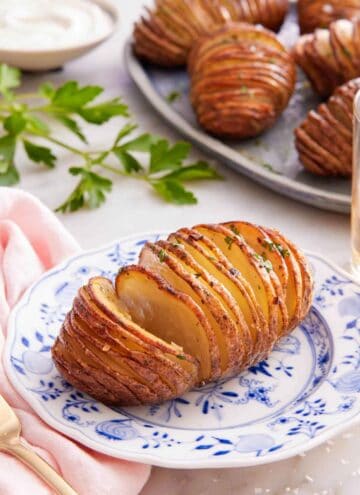 A plate with a hasselback potato with more on a platter in the background.