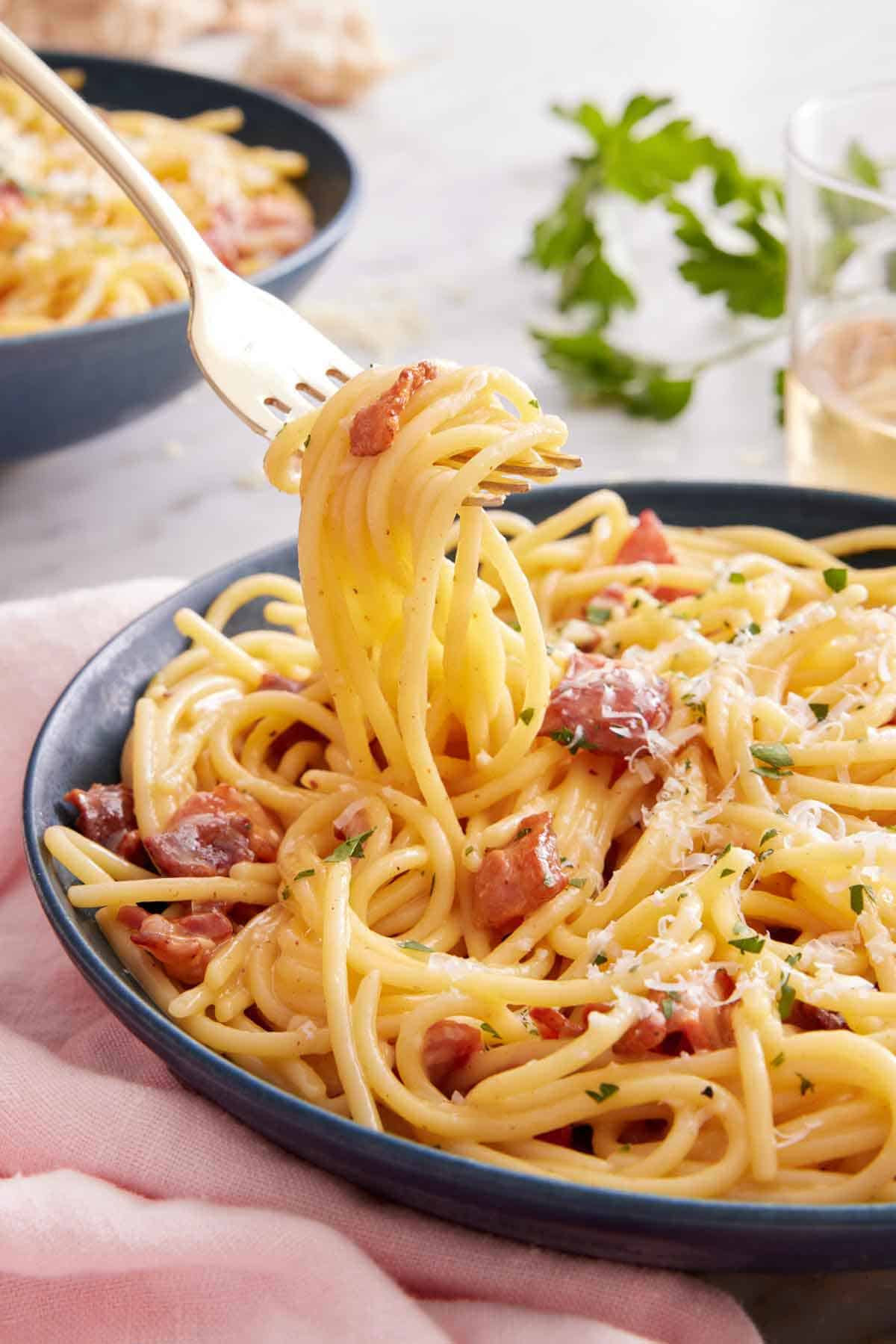 A fork lifting up noodles from a plate of pasta carbonara.