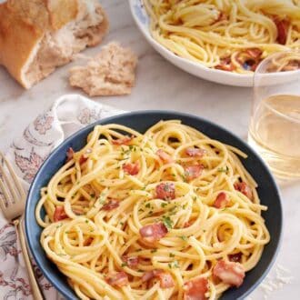 Pinterest graphic of a bowl of pasta carbonara with torn bread, glass of wine, and another plate of pasta in the background.
