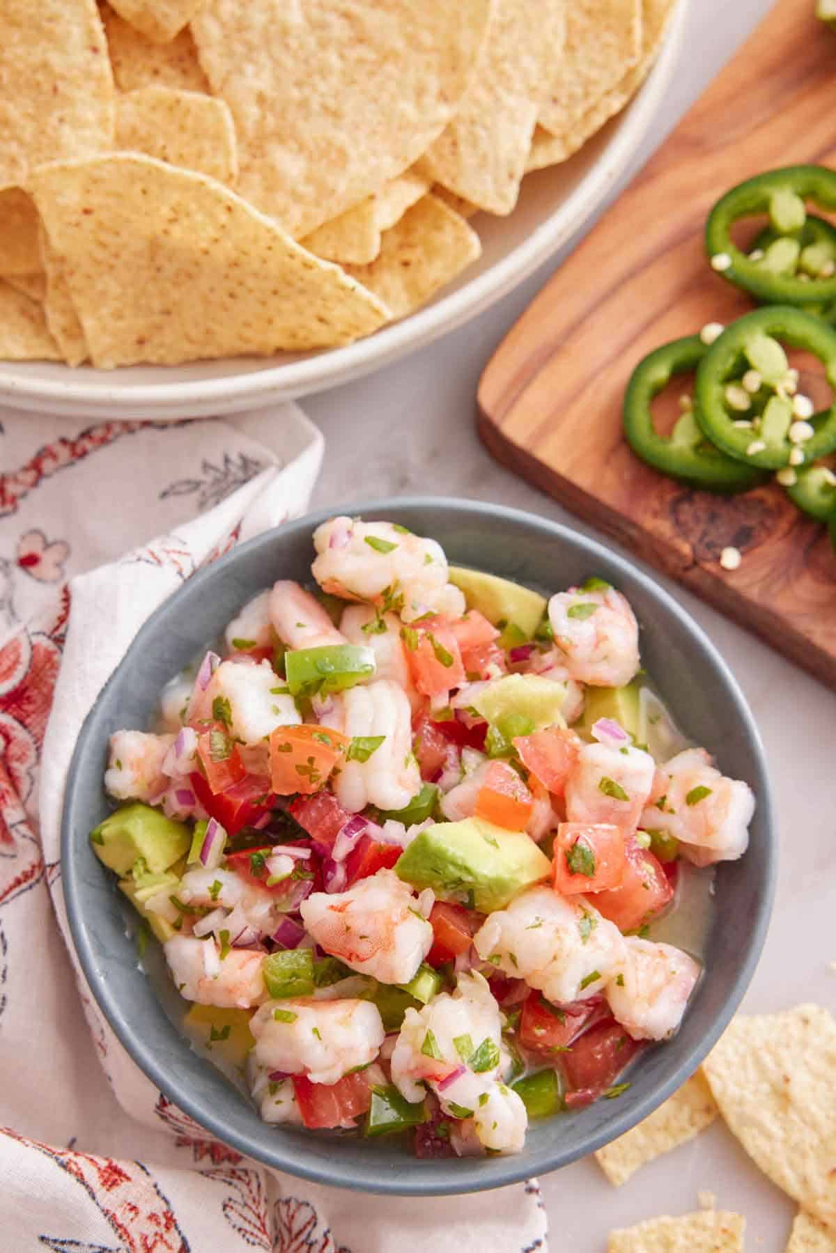 Overhead view of a bowl of shrimp ceviche with a bowl of tortilla chips and cut jalapenos beside it.