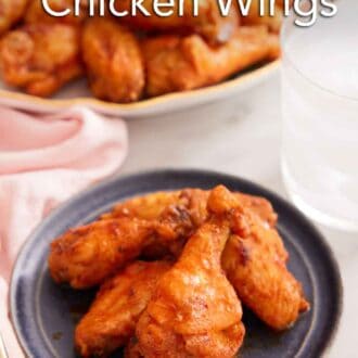 Pinterest graphic of a plate with air fryer chicken wings with a platter of more in the background with a glass of water.