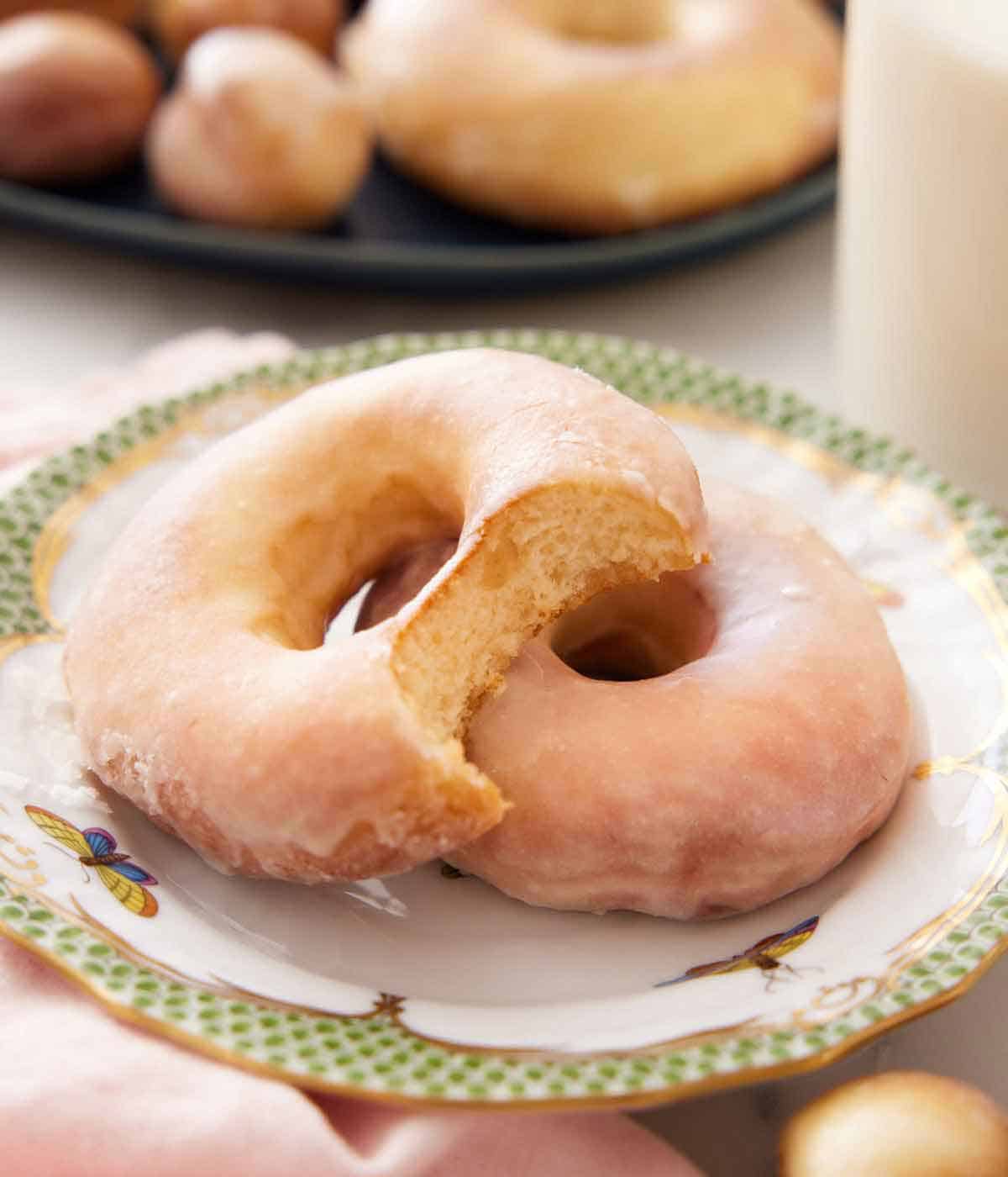 A plate with a glazed air fryer donut with a second stacked on top with a bite taken out of it.