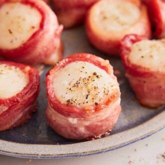 A close up view of a bacon wrapped scallop on a platter with more.
