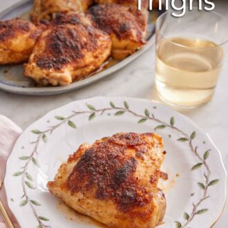 Pinterest graphic of a plate with a baked chicken thigh with a glass of wine and additional chicken thighs in the background.