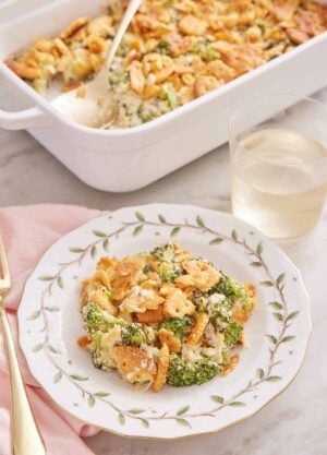 A plate with a serving of broccoli casserole with a glass of wine and baking dish in the background.