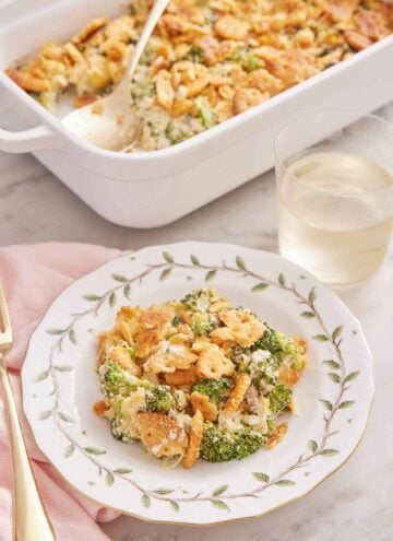A plate with a serving of broccoli casserole with a glass of wine and baking dish in the background.