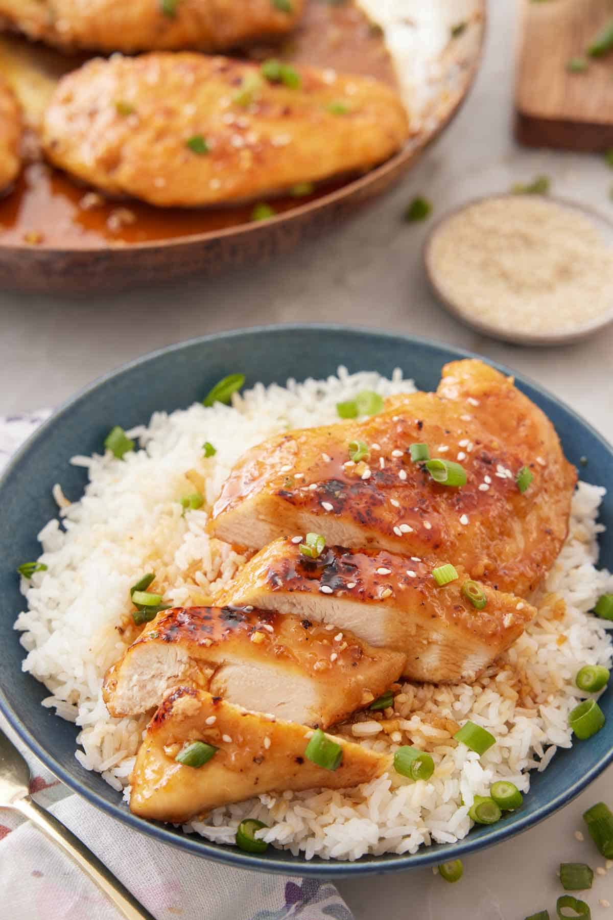 A plate of rice with a honey garlic chicken, half sliced, on top.