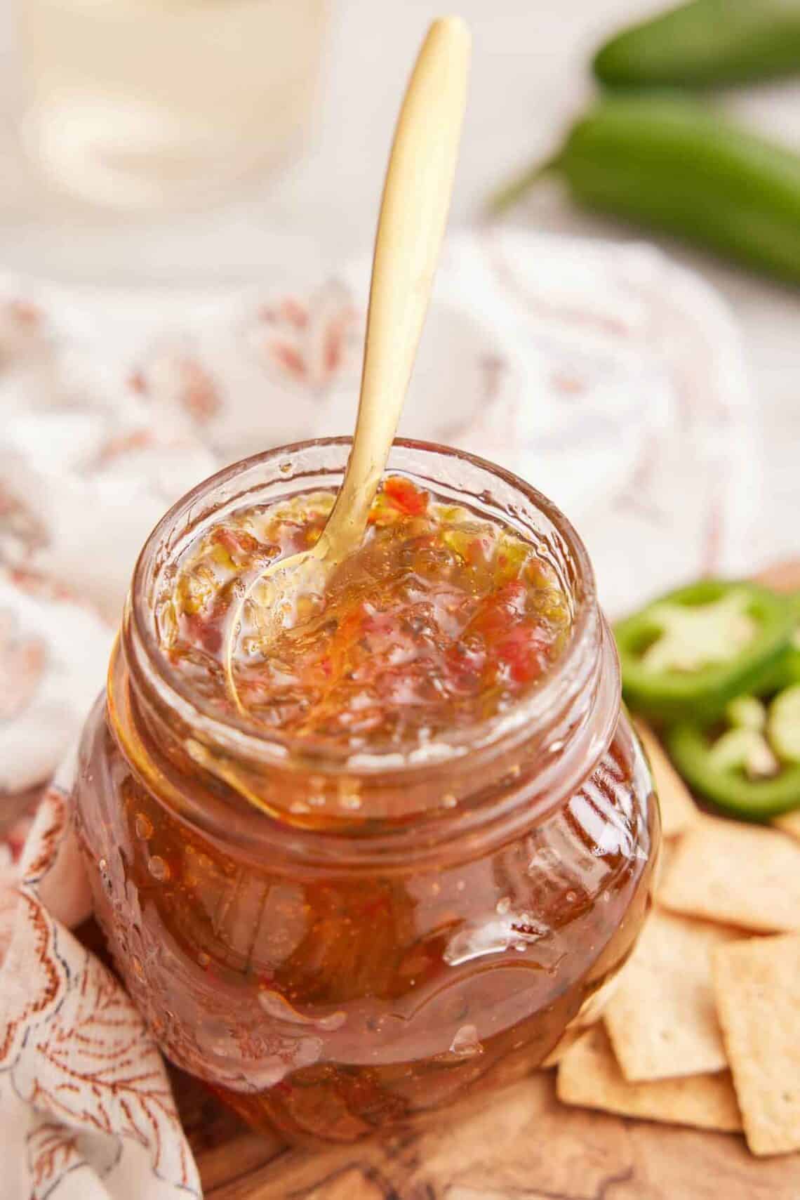 A jar of jalapeno jelly with a golden spoon inserted.