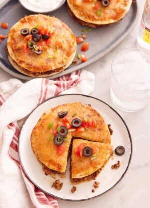 A plate with a Mexican pizza with a slice cut with a platter in the back with two more.