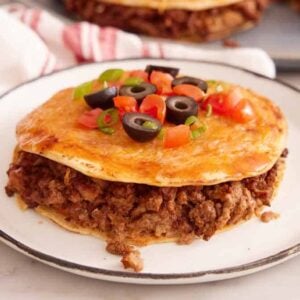 A plate with a Mexican pizza topped with chopped olives, tomatoes, and green onions.