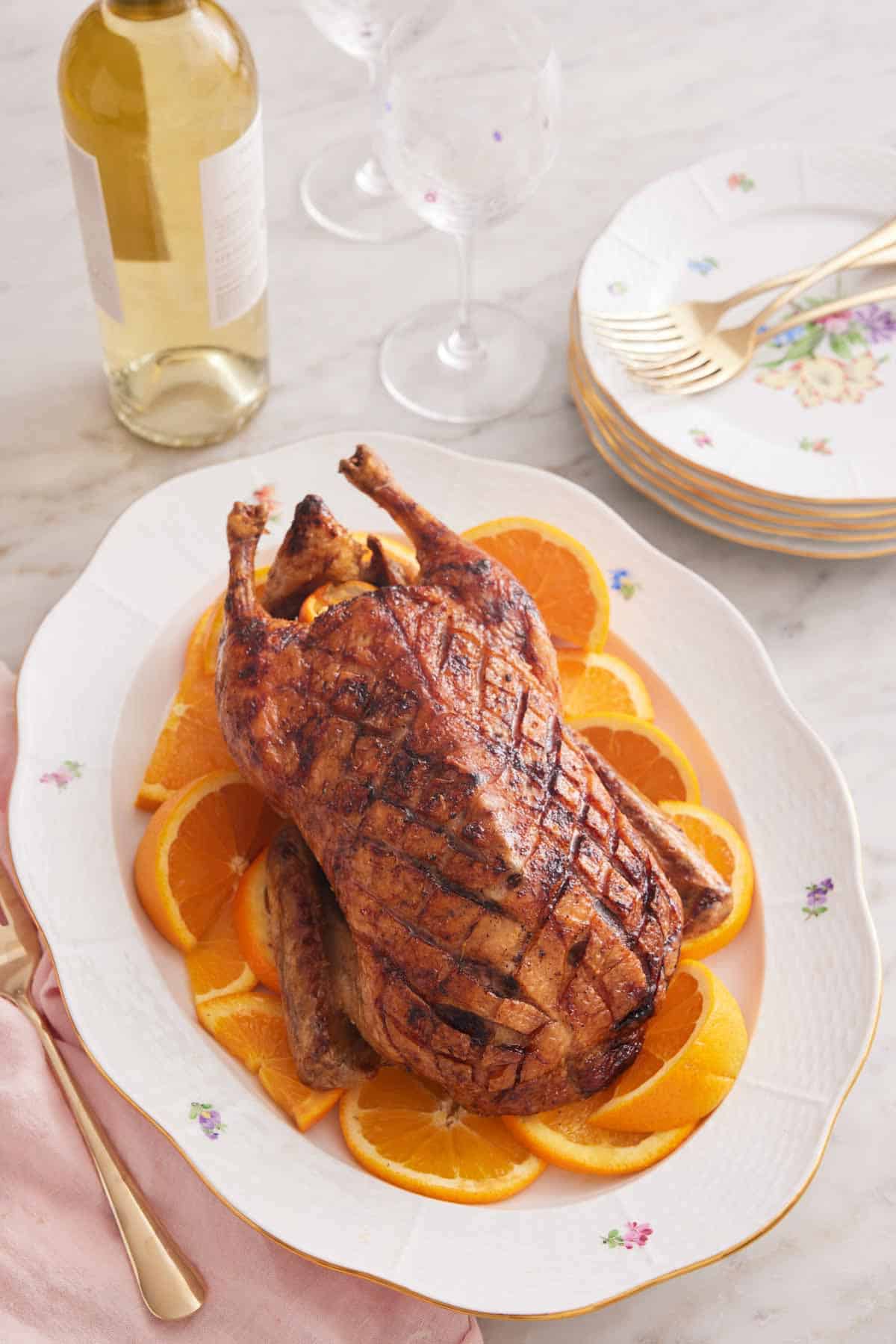 A white platter with sliced oranges with a roasted duck on top.