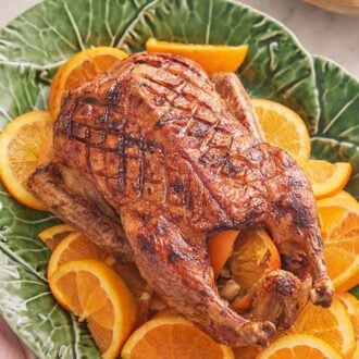 Overhead view of a green platter with a roasted duck with orange slices underneath.