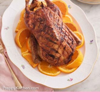 Pinterest graphic of a white platter with sliced oranges with a roasted duck on top.