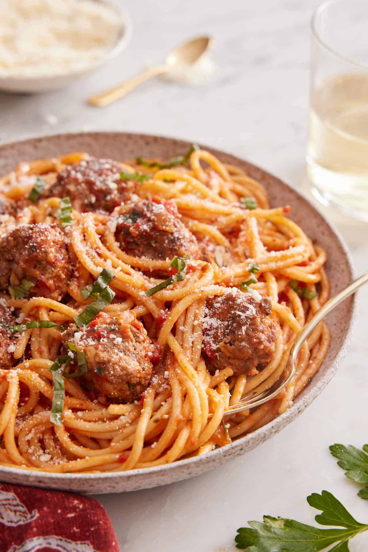 A close view of a plate of spaghetti and meatballs with a fork tucked in with a glass of wine in the back.