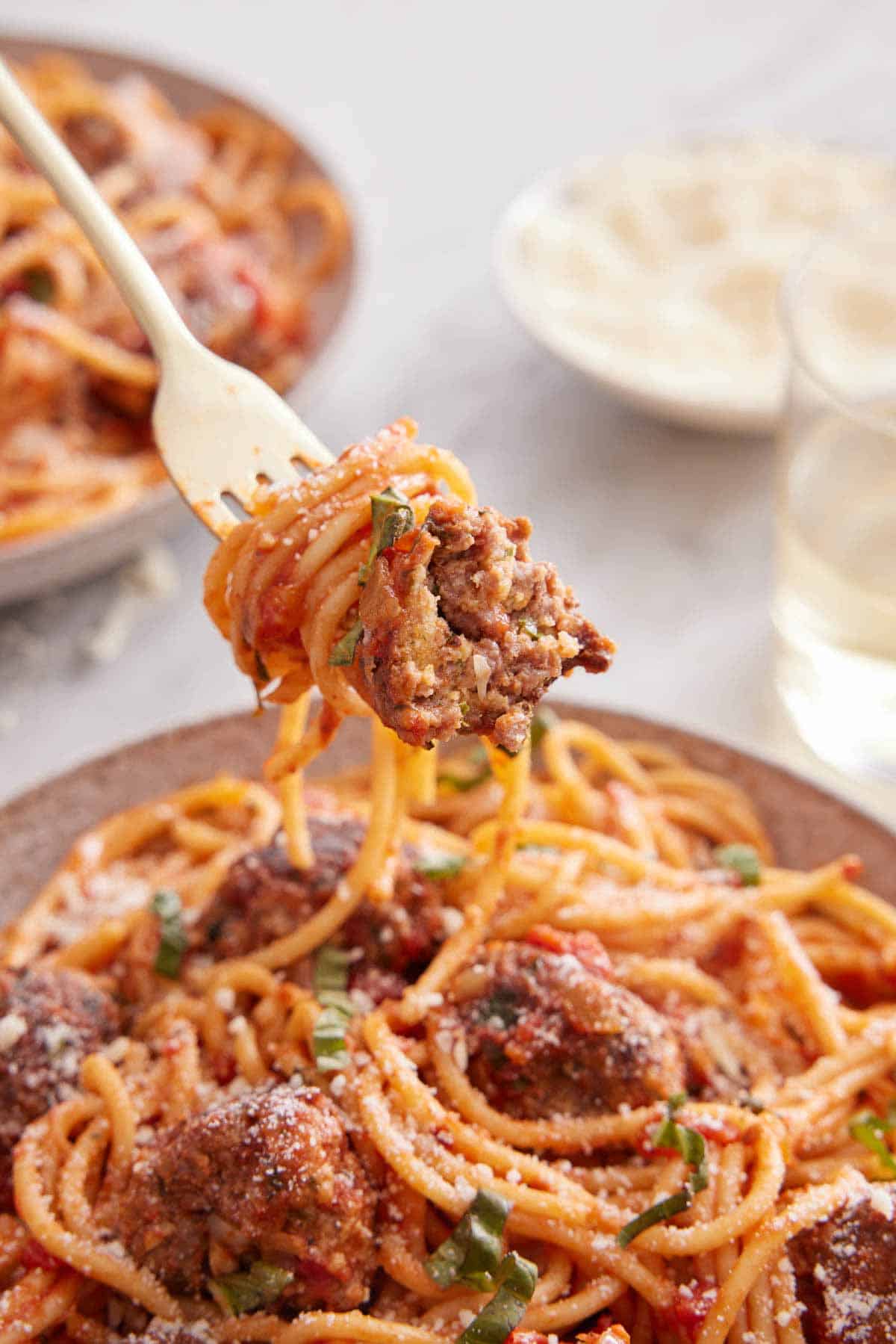 A forkful of spaghetti and meatballs lifted from a plate.