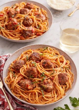 Two plates of spaghetti and meatballs with a glass of wine inbetween.