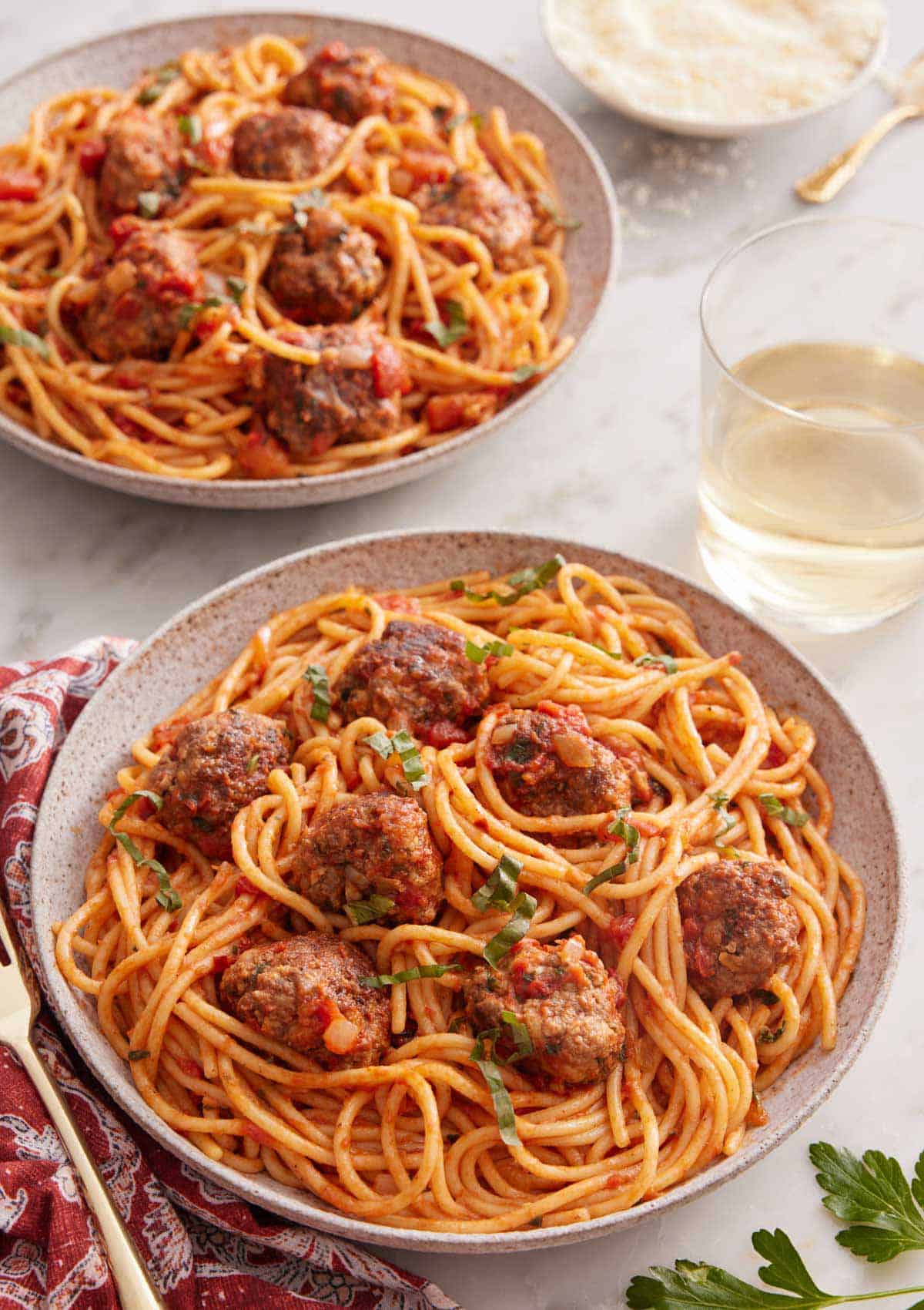 Two plates of spaghetti and meatballs with a glass of wine inbetween.