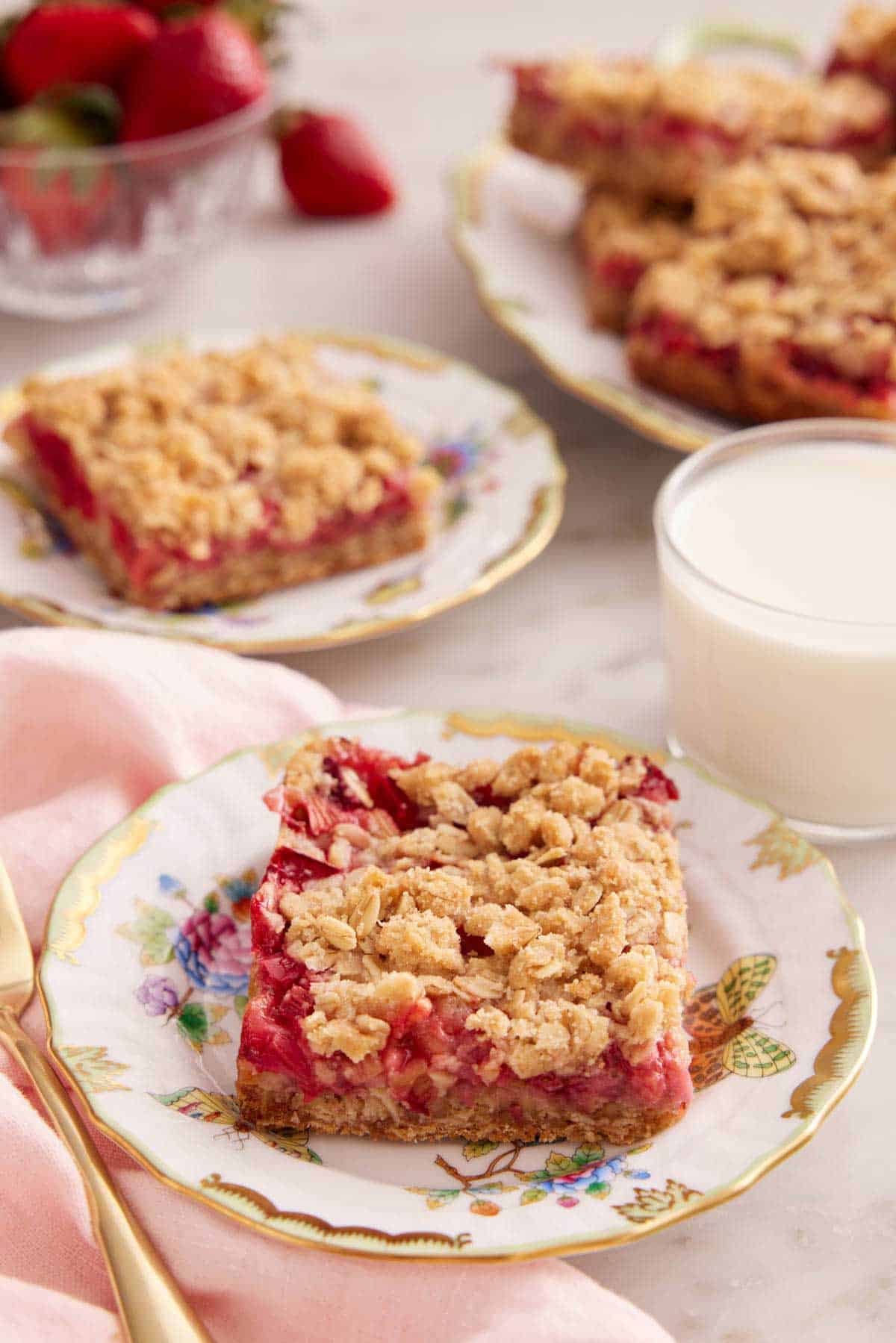 A couple plates with strawberry rhubarb bars and a glass of milk.