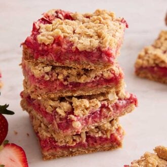 A profile view of a stack of strawberry rhubarb bars with more around it and some strawberries.