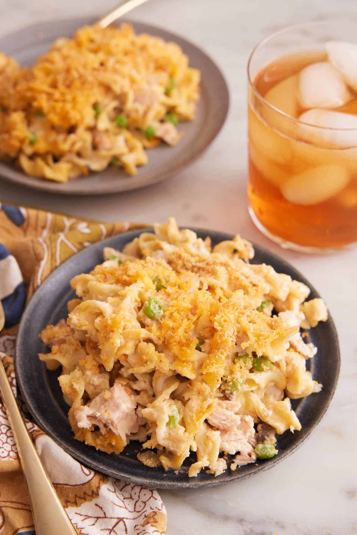 Two plates of tuna casserole with a glass of iced drink on the side.