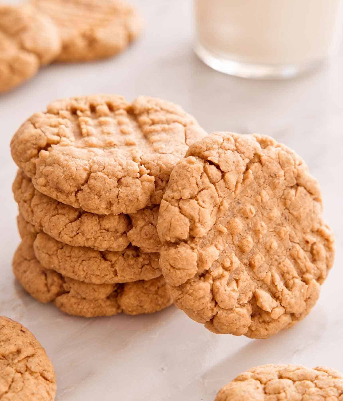 A stack of four almond butter cookies with one cookie leaning on the stack.