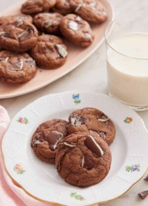 A plate with three Andes Mint Cookies with a glass of milk and platter of cookies in the background.