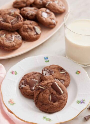A plate with three Andes Mint Cookies with a glass of milk and platter of cookies in the background.