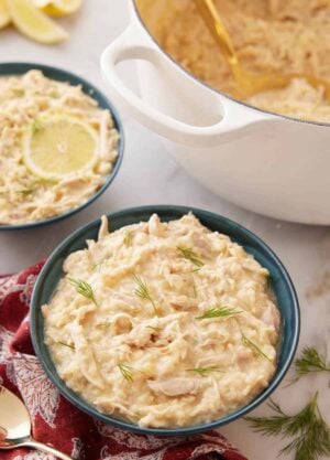 A bowl of avgolemono with a large pot and second bowl of avgolemono in the background.