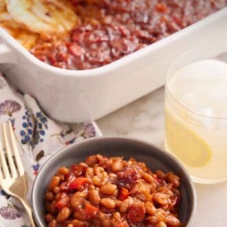 Pinterest graphic of a bowl of baked beans with a glass of lemonade and baking dish of baked beans in the background.
