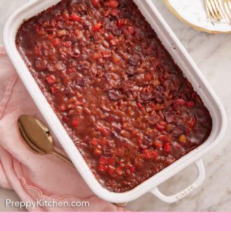 Pinterest graphic of an overhead view of a baking dish with baked beans. Stack of plates and forks to the side.