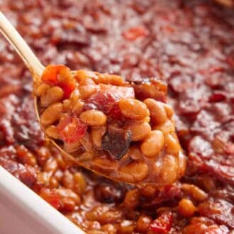 Close up view of a spoonful of baked beans lifted from a baking dish.