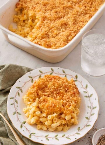 A plate of baked mac and cheese with a glass of water and baking dish with the rest in the background.