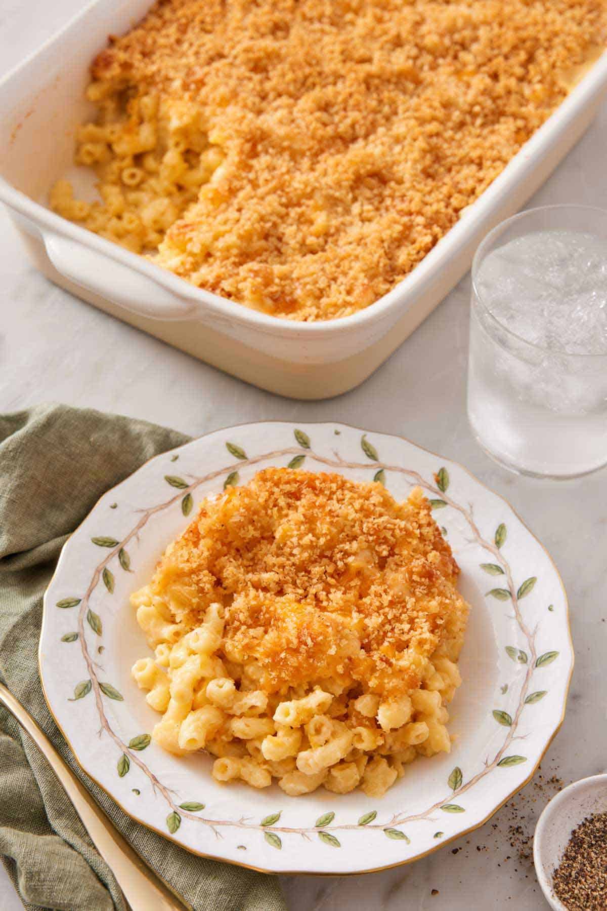 A plate of baked mac and cheese with a glass of water and baking dish with the rest in the background.