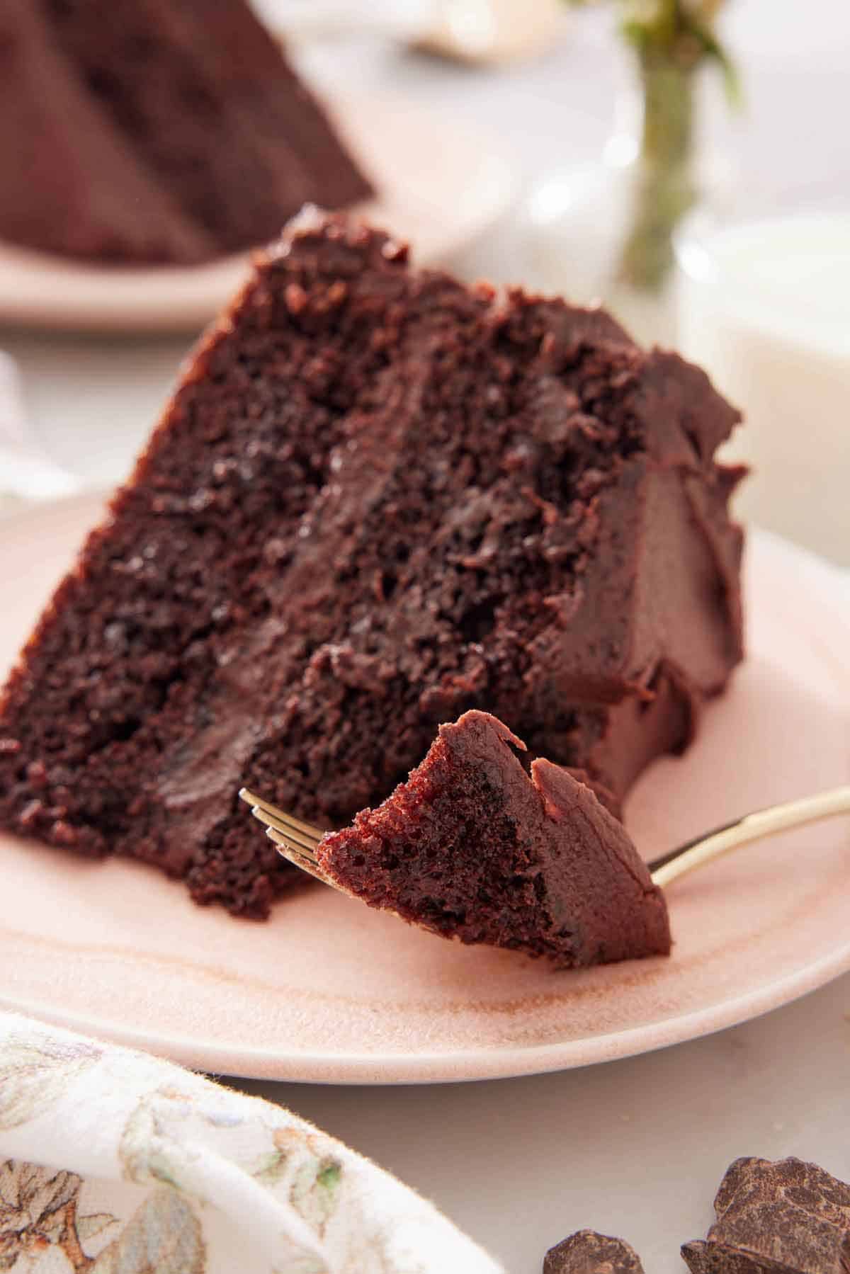 A slice of chocolate cake on a plate with a forkful in front.