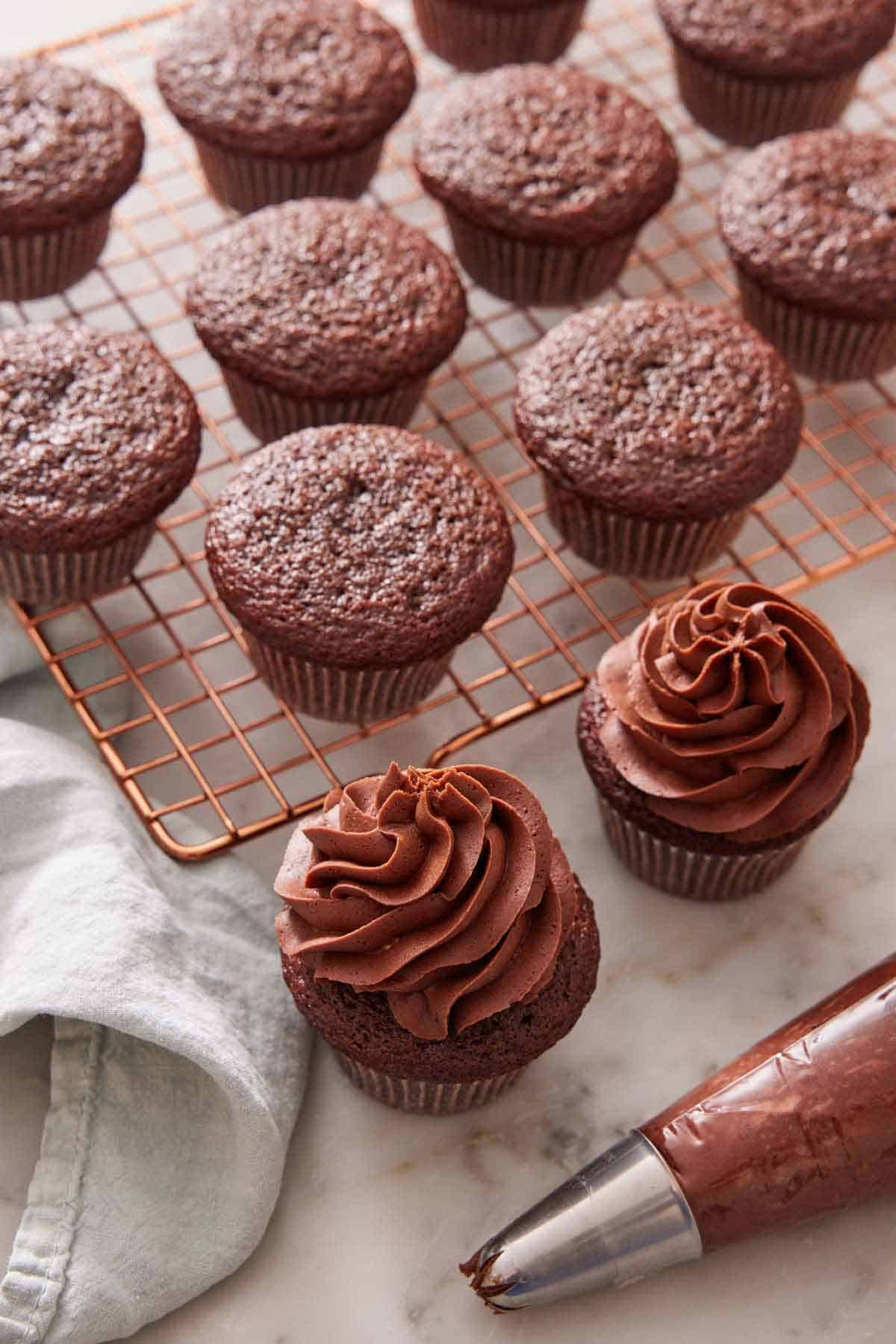 Chocolate cupcakes on a cooling rack with two frosted.