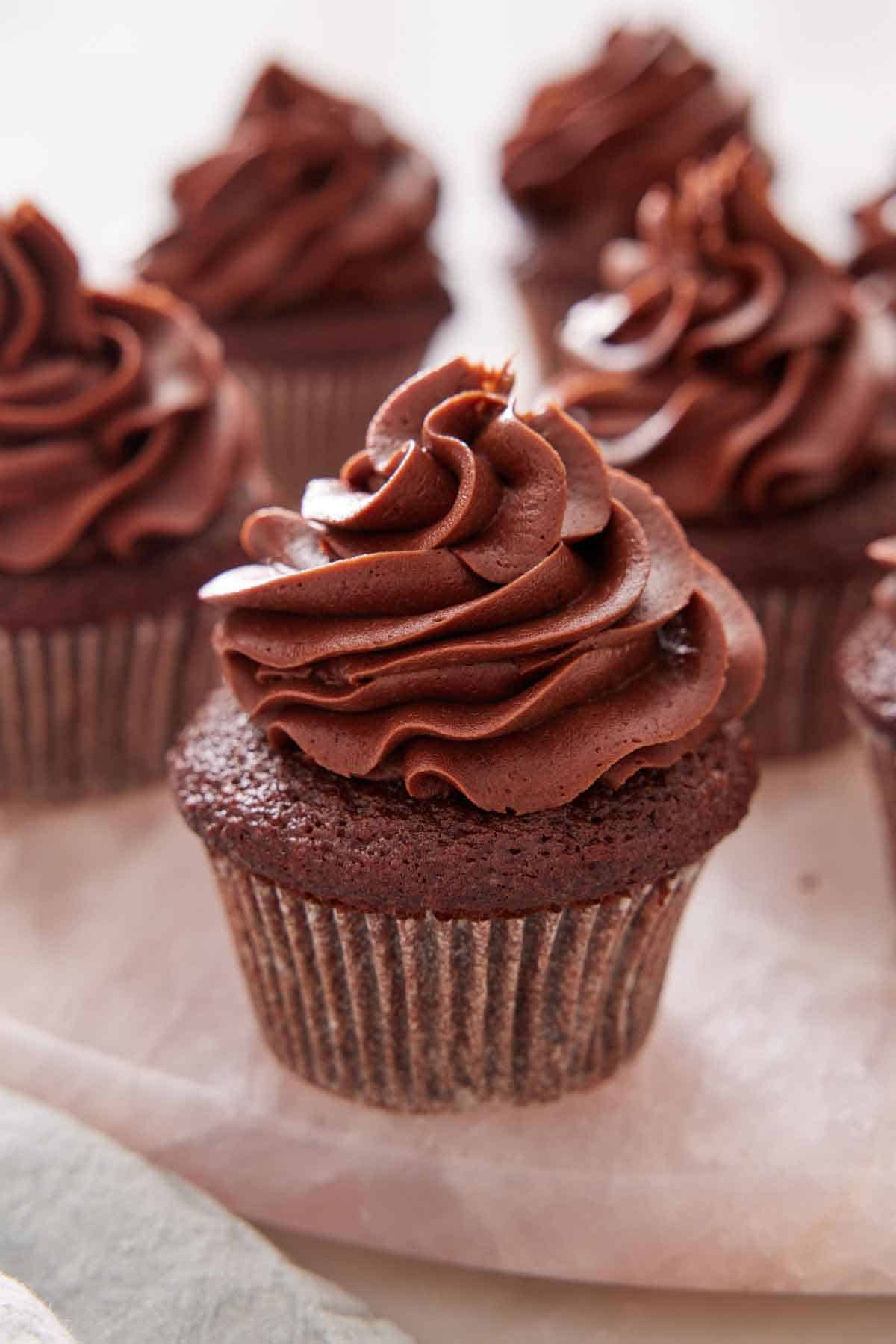 Multiple chocolate cupcakes with frosting on top with one in front.