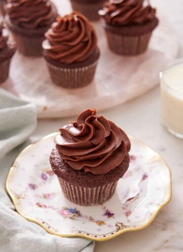 A chocolate cupcake on a plate with more on a platter in the background.