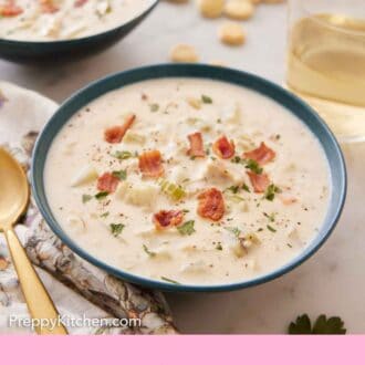 Pinterest graphic of two bowls of clam chowder with a glass of wine and some crackers in the background.