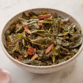 A bowl of collard greens with some torn bread in the background.