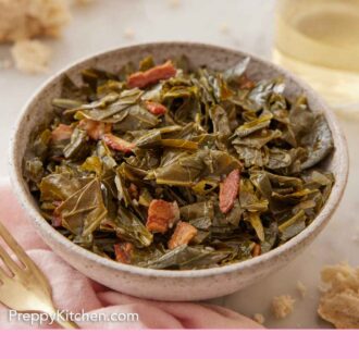 Pinterest graphic of close up view of a bowl of collard greens with a glass of wine and some torn bread in the back.