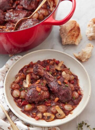 A plate of coq au vin with torn bread and a large pot in the background.