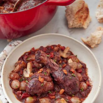 Pinterest graphic of a plate of coq au vin with torn bread and a large pot in the background.